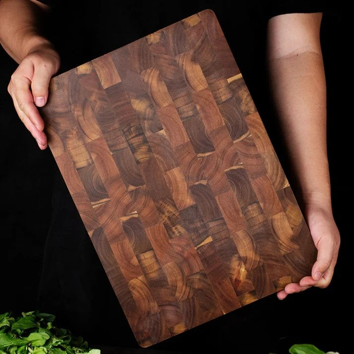 Aikona end-grain acacia cutting board held up against a dark background